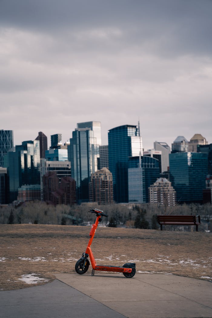 Orange electric scooter with Calgary's skyline as a backdrop on a cloudy day.