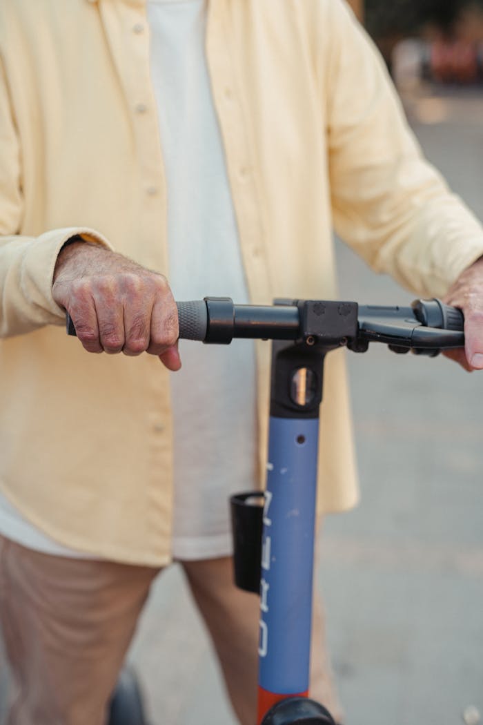 An adult riding an electric scooter outdoors, highlighting hands on handlebars.